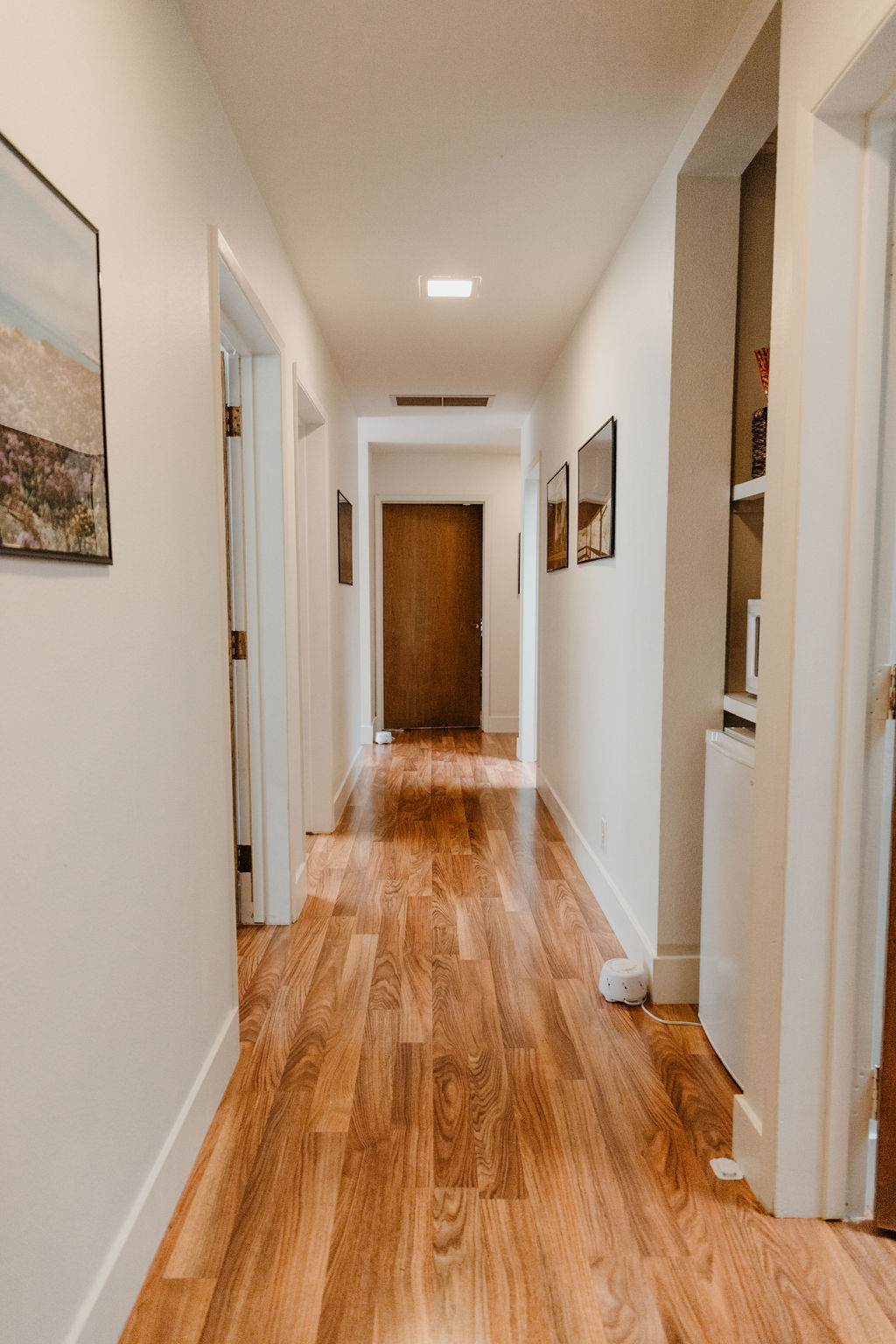 Hallway leading to therapy rooms at Coastal Therapy Group's Carlsbad office with hardwood floors and framed artwork